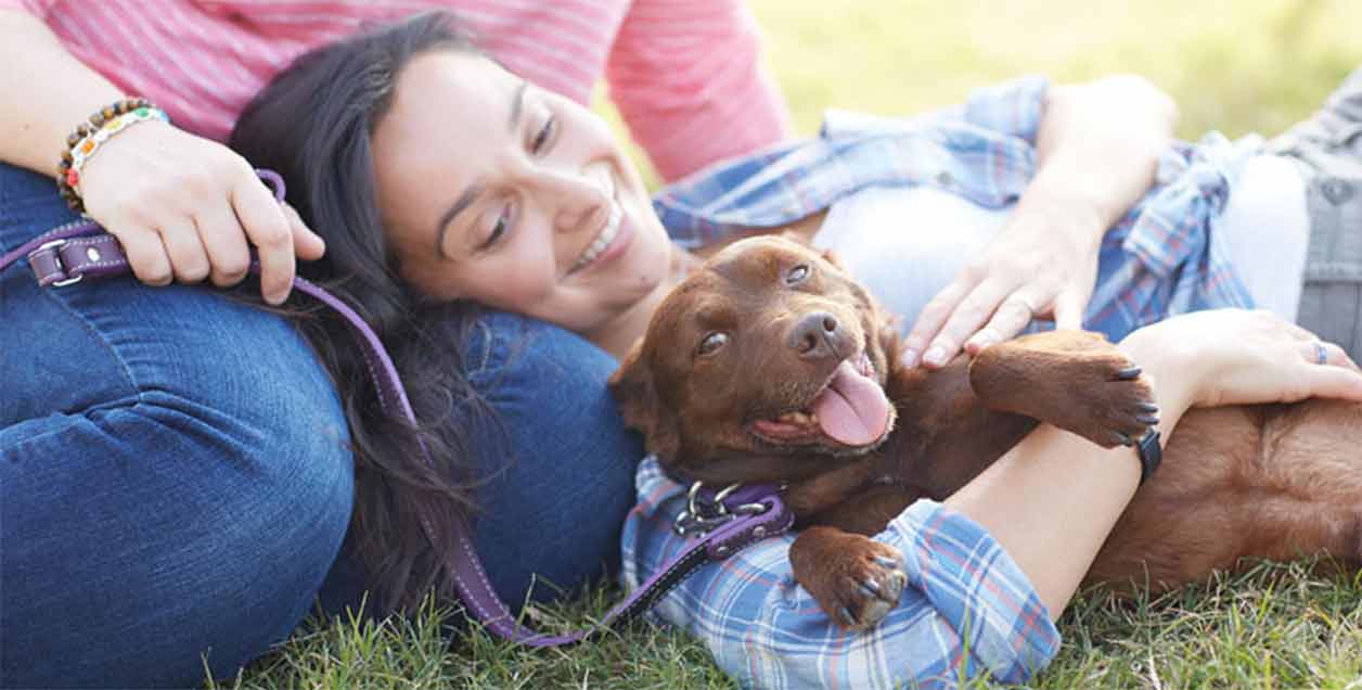 Woman laying with her dog in the grass.